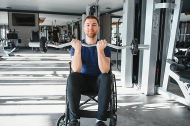Tekerlekli sandalyede otururken halterle egzersiz yapan engelli bir insan spor salonunda dayanıklılık ve güç gösterisi yapar.