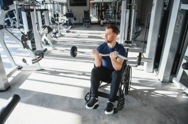 Modern spor salonunda halterle egzersiz yapan engelli bir adam rehabilitasyon sürecinde güç ve direnç gösteriyor.