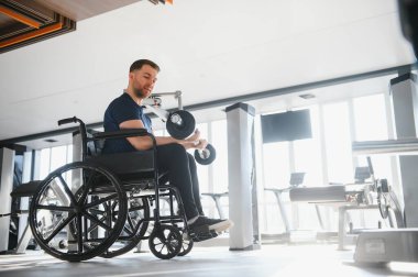 Tekerlekli sandalyedeki güçlü adam ağırlık kaldırıyor, spor salonunda egzersiz yapıyor, rehabilitasyona ve sağlığına odaklanıyor.