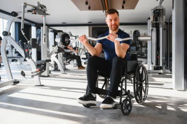 Tekerlekli sandalyede otururken halter kullanan, egzersiz yapan ve spor salonunda kas çalıştıran bir adam.