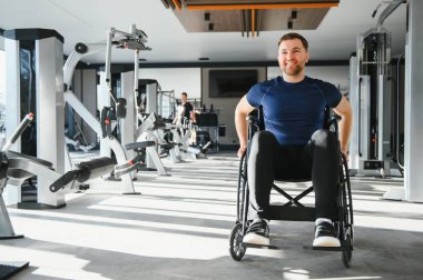 Tekerlekli sandalyedeki adam, parlak bir spor salonunda egzersiz yapıyor, engelliler için kapsayıcılık ve aktif yaşam tarzını destekliyor.