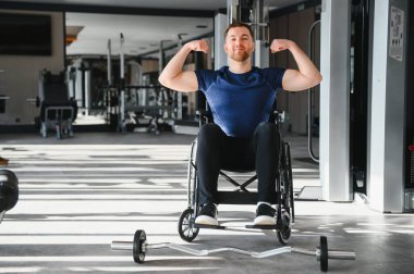 Özürlü bir sporcu, modern spor salonunda tekerlekli sandalyede otururken kaslarını esneterek rehabilitasyon veya adaptasyon süresince güç ve kararlılık gösteriyor.