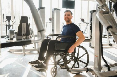 Adam spor salonunda tekerlekli sandalye egzersizi yapıyor, azim gösteriyor ve engelli insanlar için sağlıklı yaşam tarzını teşvik ediyor.