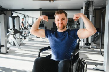 Spor salonunda rehabilitasyon için egzersiz yapan güçlü bir sporcu, pazılarını ve gülümsemesini gösteriyor, sağlıklı bir yaşam tarzını destekliyor ve fiziksel sınırlamaların üstesinden geliyor.