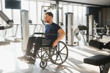 Spor salonunda tekerlekli sandalye egzersizi yapan genç bir adam rehabilitasyon ve sporda azim ve katılımın gücünü gösteriyor.