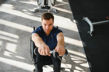 Tekerlekli sandalyedeki kararlı adam, kablo yayını makinesini kullanıyor. Erişilebilir spor salonundaki rehabilitasyon sırasında güç ve dayanıklılık gösteriyor.