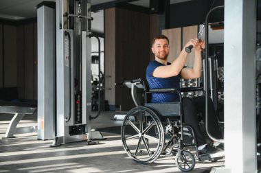 Tekerlekli sandalyedeki gülen adam spor salonunda kablo kullanarak egzersiz yapıyor rehabilitasyon sırasında kararlılık ve güç gösteriyor.