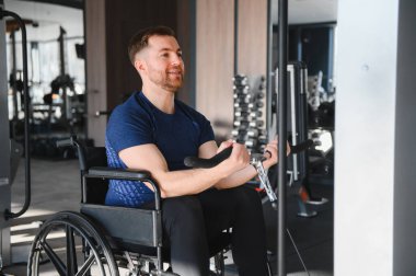Kollarını spor salonunda ağırlık makinesiyle çalıştıran engelli bir adam rehabilitasyon ve fizik tedavi üzerine çalışıyor.