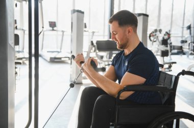 Spor salonunda kollarını ağırlık makinesiyle çalıştıran engelli bir kişi rehabilitasyon tedavisi görüyor.