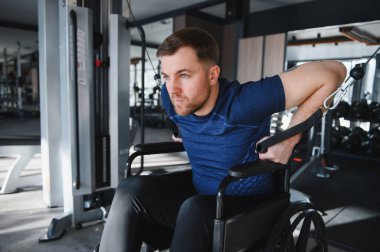 Spor salonunda kablo makinesiyle egzersiz yapan engelli bir adam rehabilitasyon sürecinde kararlılık ve güç gösteriyor.