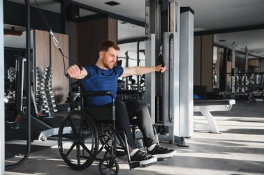 Adam spor salonunda rehabilitasyon egzersizlerine katılıyor, gücü arttırmak ve iyileşmeyi hızlandırmak için kablo makinesini kullanıyor.