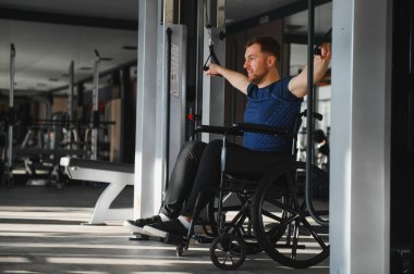 Tekerlekli sandalyedeki adam spor salonunda kablo ağırlıklarıyla egzersiz yapıyor, dayanıklılık gösteriyor ve adapte olmuş antrenmanlarla fitness hedefleri peşinde koşuyor.