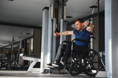 Tekerlekli sandalyedeki adam spor salonunda ağırlık çalışıyor, rehabilitasyona ve fizik tedaviye odaklanıyor.
