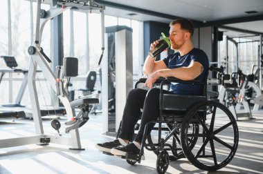 Engelli biri spor salonunda egzersiz yaptıktan sonra protein içeceği içiyor, kapsayıcılığı ve aktif yaşam tarzını destekliyor.