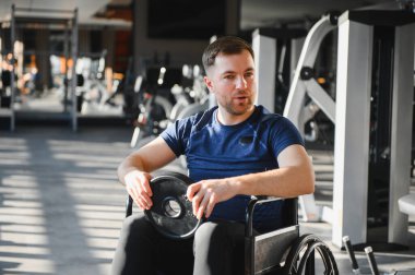 Engelli biri spor salonunda tekerlekli sandalyede ağırlık egzersizi yapıyor, buna dahil olma ve uyum sağlama eğitimi veriyor.