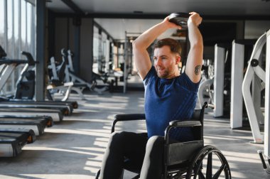 Tekerlekli sandalyedeki adam spor salonunda ağırlık kaldırıyor, fitness ve rehabilitasyona odaklanıyor. Güç ve kararlılığı vurgular