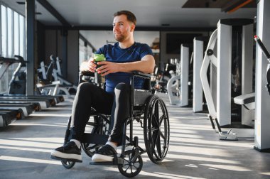 Özürlü bir sporcu spor yapmaya ara verir. Elinde bir spor içeceği tutarken, modern bir spor salonunda tekerlekli sandalyesinde oturur.