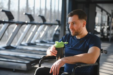 Tekerlekli sandalyede dinlenen ve sallanan bir adam spor salonunda antrenman yaptıktan sonra fiziksel kısıtlamaların üstesinden gelmek için azim ve azim gösteriyor.