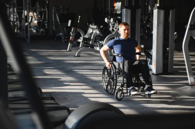 Tekerlekli sandalyedeki adam ulaşılabilir spor salonunda egzersiz yapıyor, kapsayıcılığını gösteriyor ve rehabilitasyon ve spor eğitimi yoluyla aktif yaşam tarzını sürdürüyor.
