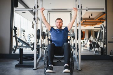 Halterle egzersiz yapan engelli bir adam, ulaşılabilir spor salonundaki rehabilitasyon eğitiminde direnç ve güç gösterisi yapıyor.