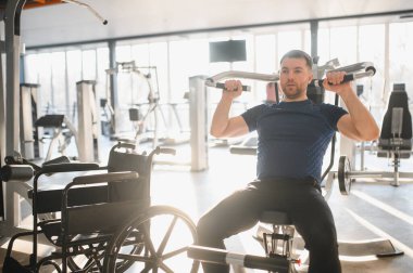 Tekerlekli sandalyesiyle spor salonundaki bir makinede egzersiz yapan üst vücut gücü ve rehabilitasyon üzerine çalışan biri.