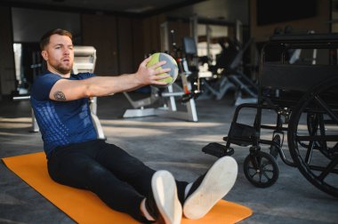 Spor salonundaki rehabilitasyon egzersizleri için ilaç topunu kullanan bir adam fitness ve iyileşmeye olan bağlılığını gösteriyor.