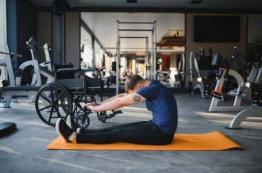 Beden eğitiminde yoga minderinde gerinen engelli bir adam fiziksel zorluklara rağmen rehabilitasyona ve forma bağlılığını gösteriyor.