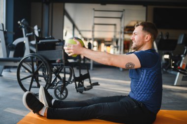 Tekerlekli sandalyedeki bir adam spor salonunda rehabilitasyon seansına aktif olarak katılıyor, sağlık ve iyileşme üzerine yoğunlaşıyor.