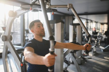 Sırt üstü uçan makine kullanan kararlı erkek sporcu, modern spor salonunda vücut gücü ve rehabilitasyon üzerine çalışıyor.