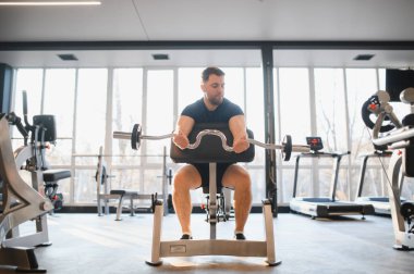 Tekerlekli sandalyedeki kararlı erkek sporcu, modern rehabilitasyon salonundaki kasları güçlendirmek için ağırlık kullanıyor. İyileşme ve zindelik için adaptasyon eğitimi veriyor.