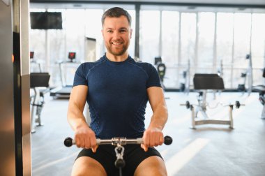 Gülümseyen sporcu, modern bir spor salonunda sırt kaslarını çalıştırıyor. Güç antrenmanına ve forma odaklanıyor.