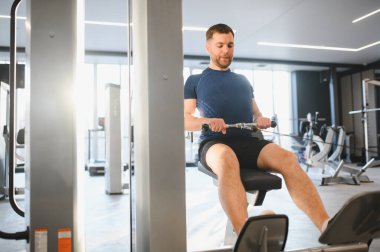 Kablo sıra makinesi kullanan kararlı bir adam modern bir spor salonunda rehabilitasyon programının bir parçası olarak sırt kaslarını güçlendiriyor.
