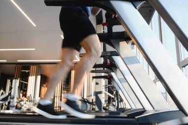 Hasta koşu bandında koşuyor, rehabilitasyon sırasında spor salonunda bacak egzersizi yapıyor, iyileşmeyi ve fizik tedaviyi destekliyor.