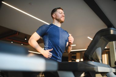 Koşu bandında koşan kararlı erkek sporcu, spor yapıyor ve modern spor salonundaki sakatlığını atlatıyor.