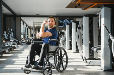 Tekerlekli sandalyedeki adam spor salonunda kendine güvenerek kaslarını esnetiyor, rehabilitasyon ve engelliler için dayanıklılık eğitimini vurguluyor.