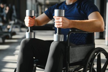 Tekerlekli sandalyede egzersiz yaparken dambıl kullanan kararlı sporcu rehabilitasyon eğitiminde direnç ve güç gösteriyor.