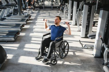 Tekerlekli sandalyedeki dambıllarla egzersiz yapan, dayanıklılık, dayanıklılık gösteren ve modern spor salonlarına dahil edici bir spor salonu sunan bir adam.