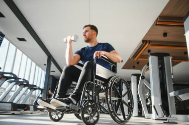 Tekerlekli sandalyedeki kararlı adam halteri kaldırıyor, egzersiz yapıyor ve spor salonunda rehabilitasyona gidiyor.