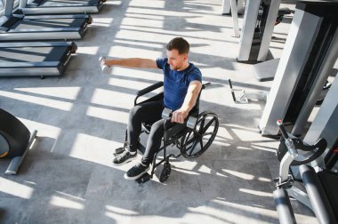 Modern spor salonunda dambıllarla egzersiz yapan, rehabilitasyondan geçen ve güç ve azim gösteren bir adam.