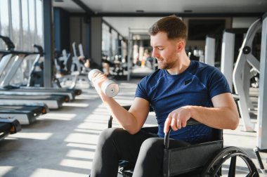 Tekerlekli sandalyedeki engelli sporcu spor salonundaki rehabilitasyon sırasında ağırlık kaldırıyor. Güç ve azim gösteriyor.