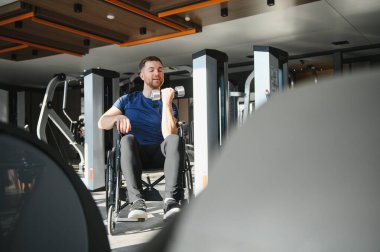 Modern bir spor salonunda dambıllarla egzersiz yapan engelli bir adam rehabilitasyona ve spor eğitimine bağlılığını gösteriyor.