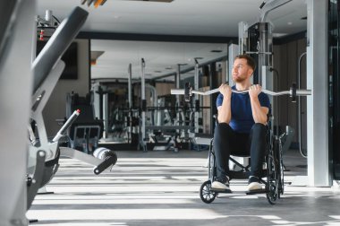 Tekerlekli sandalye kullanan, spor salonunda ağırlık kaldıran, spor rehabilitasyonunu ve güç eğitimini vurgulayan biri.