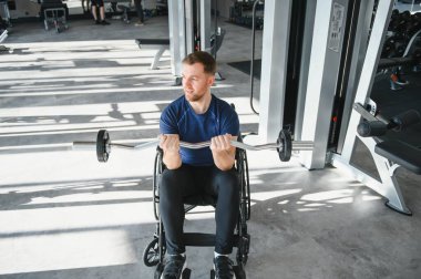 Tekerlekli sandalyede ağırlık kaldıran, modern spor salonunda egzersiz yapan, rehabilitasyon gören ve sportmenlik sergileyen erkek sporcu.