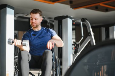 Tekerlekli sandalyede ağırlık kaldıran engelli bir sporcu modern spor salonundaki rehabilitasyon egzersizleri sırasında kollarını güçlendiriyor.