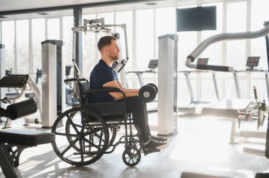 Tekerlekli sandalyede ağırlık kaldıran, egzersiz yapan ve rehabilitasyon sırasında güç toplayan bir adam.