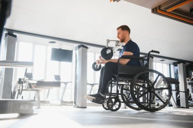 Spor salonundaki rehabilitasyon terapisi sırasında hasta ağırlıklarıyla egzersiz yapıyor. Fiziksel zorlukların üstesinden gelme azmi ve gücünü gösteriyor.