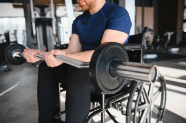 Tekerlekli sandalyedeki kişi spor salonunda halter egzersizleri yapıyor. Güç, rehabilitasyon ve kararlılık vurgulanıyor.