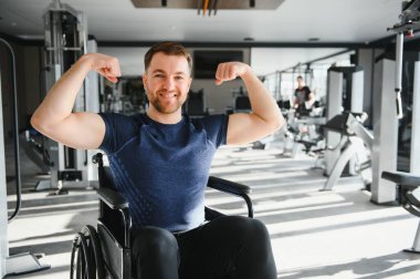 Omurilik zedelenmesi olan güçlü bir sporcu tekerlekli sandalyede oturuyor ve rehabilitasyon sırasında egzersiz yaparken pazılarını gösteriyor.