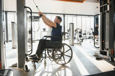 Engelli biri rehabilitasyon için spor aletlerini kullanır. Parlak, ferah bir fitness merkezinde güç ve hareket kabiliyetini geliştirmeye odaklanır.