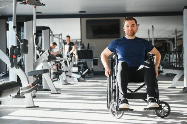 Modern spor salonunda tekerlekli sandalyede egzersiz yapan engelli bir adam rehabilitasyon sürecinde azim ve güç gösteriyor.